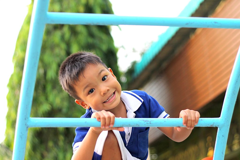 Happy asian child boy playing and climbing a steel bar toy at the playground