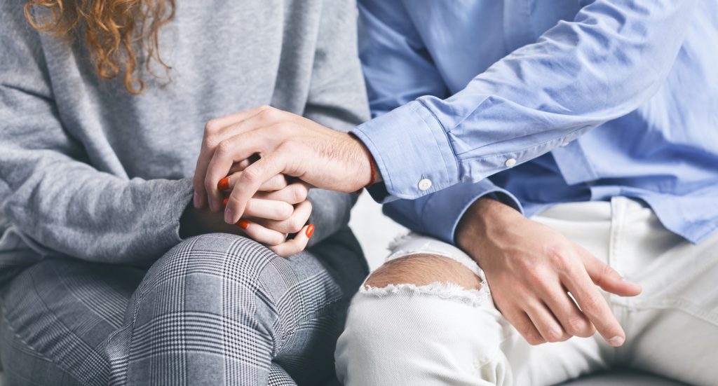 Man holding hand of stressed woman at rehab meeting